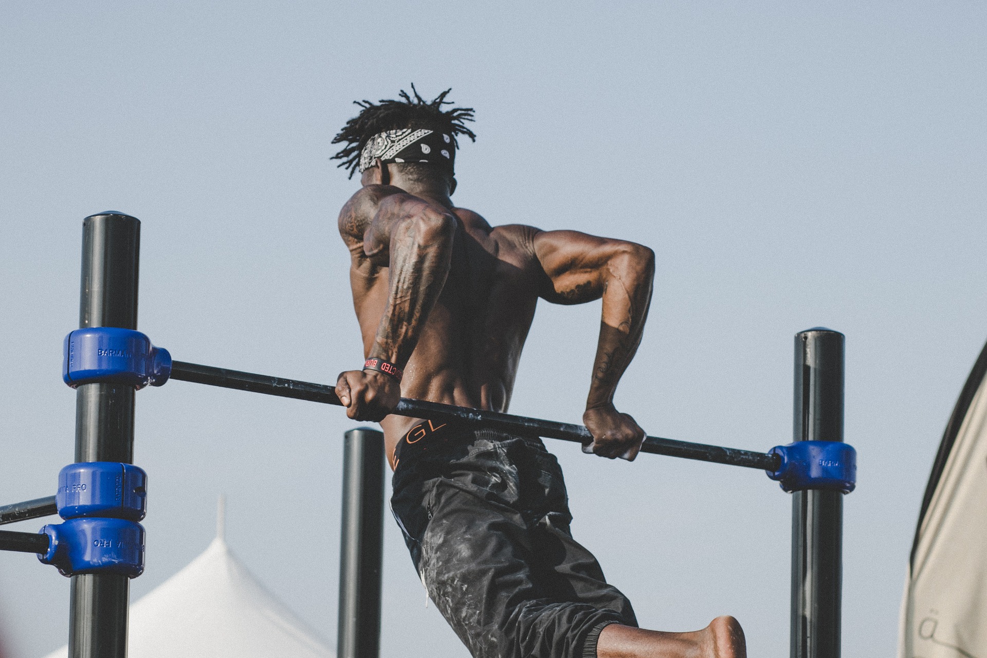 Imagem de um atleta treinando tríceps na barra fixa através de calistenia. O atleta está sem camisa e tem cabelo com dread.