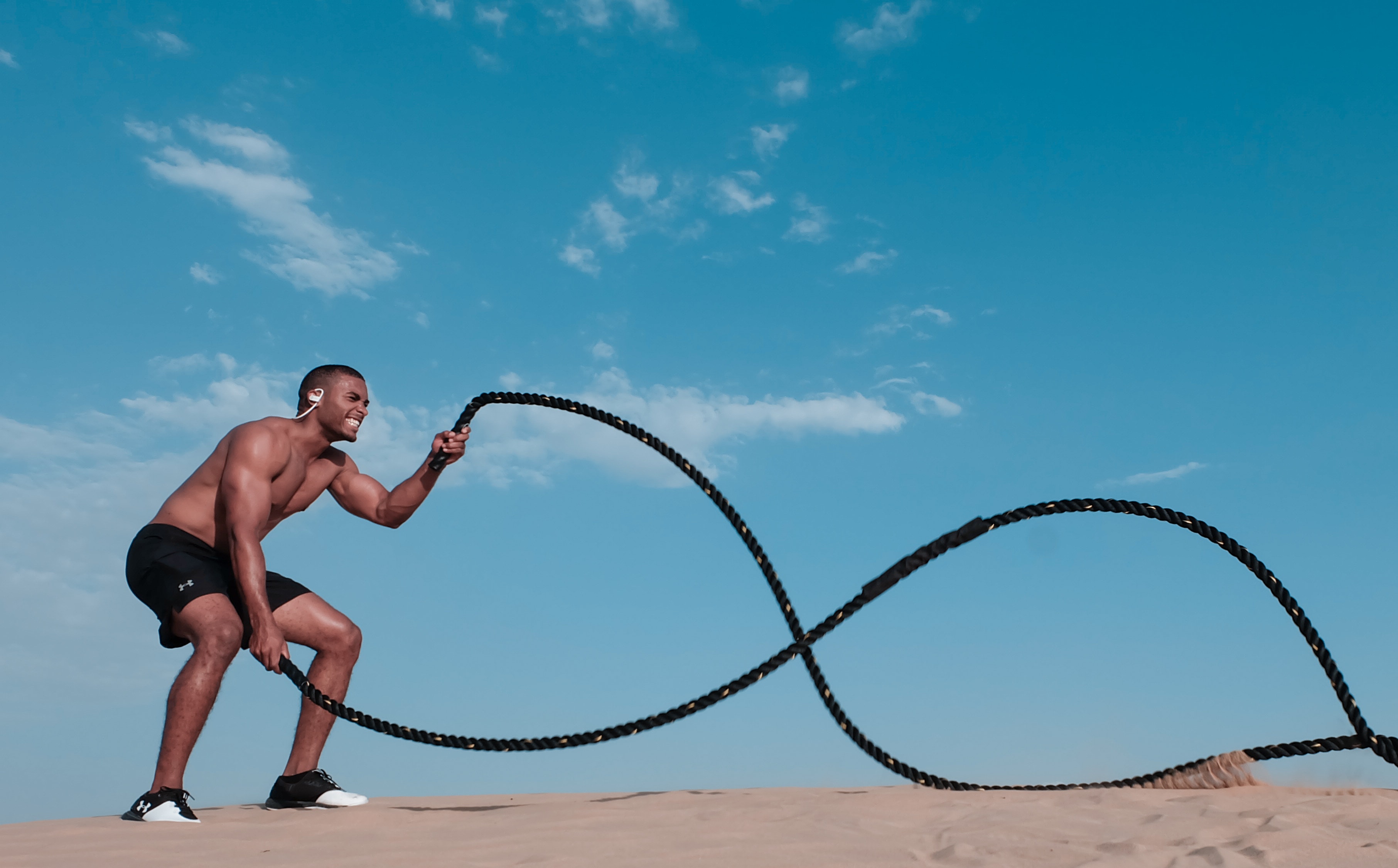 Imagem de um atleta com fone de ouvidos e sem camisa fazendo o exercicio corda naval dupla.